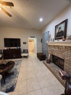 tiled living area with a brick fireplace and a ceiling fan