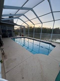 pool at dusk with an outdoor pool, glass enclosure, and a patio