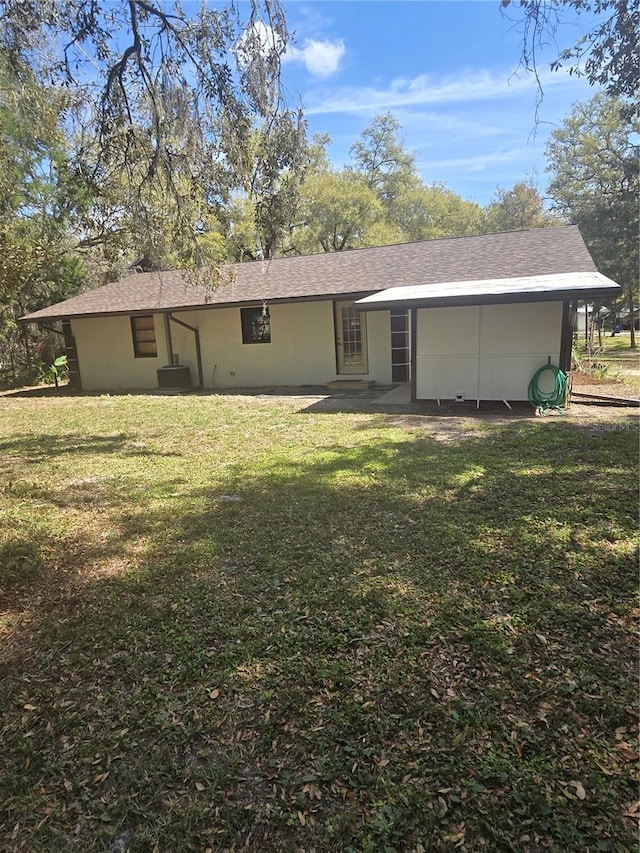 rear view of house featuring a lawn and roof with shingles