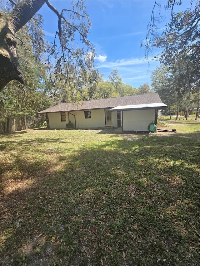 back of property with stucco siding, a shingled roof, and a yard
