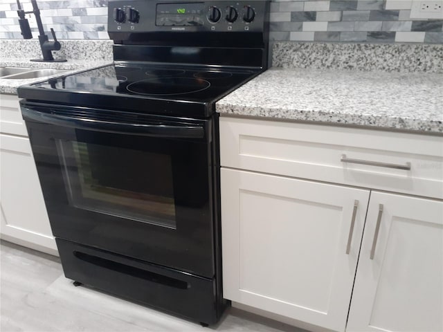 26 Clintwood Ave, Englewood, FL 34223 - kitchen with black range with electric cooktop, backsplash, white cabinets, light stone countertops, and light wood-type flooring