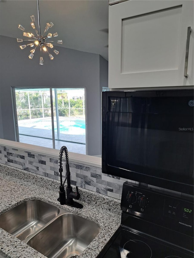 26 Clintwood Ave, Englewood, FL 34223 - kitchen with black appliances, tasteful backsplash, white cabinetry, and light stone counters