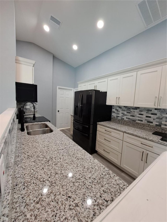 26 Clintwood Ave, Englewood, FL 34223 - kitchen featuring black refrigerator with ice dispenser, white cabinets, lofted ceiling, tasteful backsplash, and light stone countertops