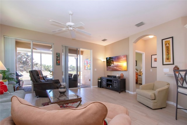 living area featuring visible vents, baseboards, ceiling fan, arched walkways, and light wood-style floors
