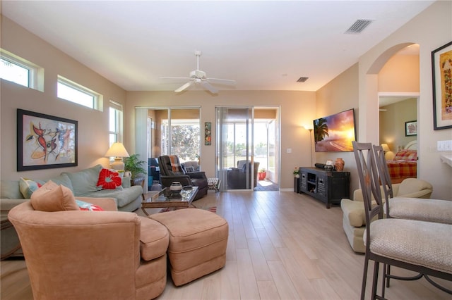 living room featuring light wood finished floors, baseboards, visible vents, arched walkways, and ceiling fan