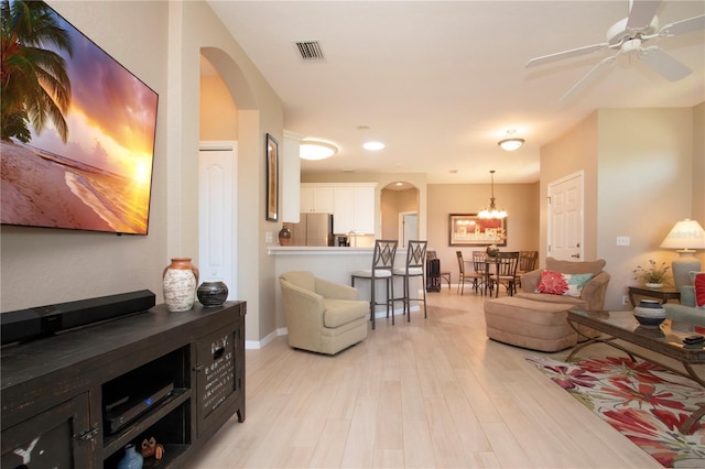 living room with light wood finished floors, baseboards, ceiling fan with notable chandelier, visible vents, and arched walkways