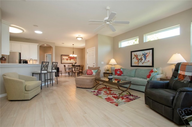 living area featuring light wood finished floors, ceiling fan with notable chandelier, and arched walkways