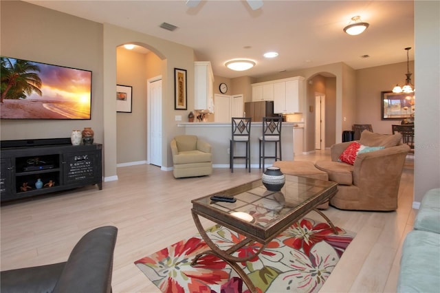 living room featuring arched walkways, light wood finished floors, and visible vents