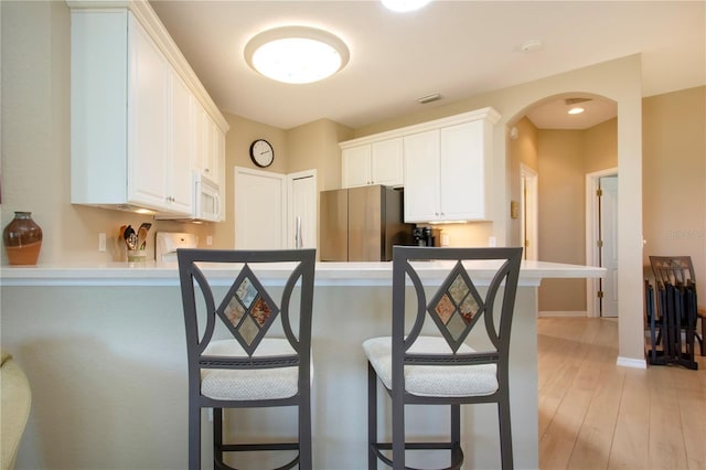 kitchen with freestanding refrigerator, a kitchen bar, a peninsula, arched walkways, and white microwave