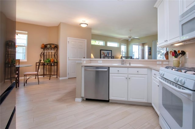 kitchen with white cabinetry, light countertops, white appliances, a sink, and a peninsula