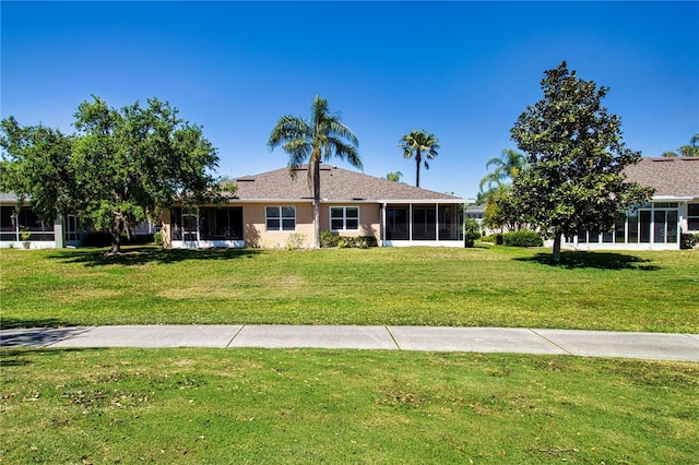 rear view of house featuring a sunroom, stucco siding, and a yard