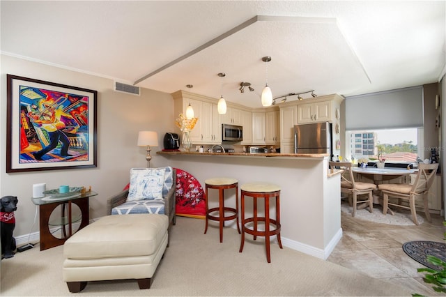 kitchen featuring visible vents, a breakfast bar area, a peninsula, cream cabinets, and stainless steel appliances