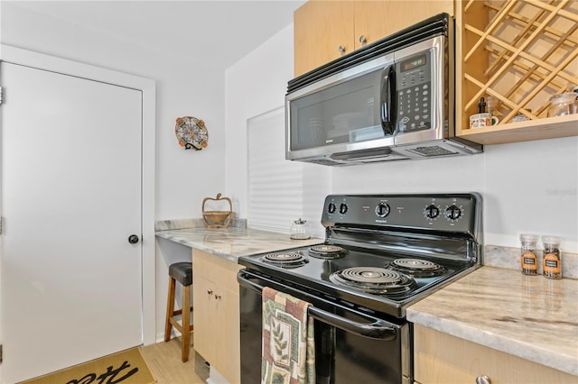 819 11th St N, Saint Petersburg, FL 33705 - kitchen featuring stainless steel microwave, light brown cabinetry, light stone counters, light wood-style flooring, and black / electric stove