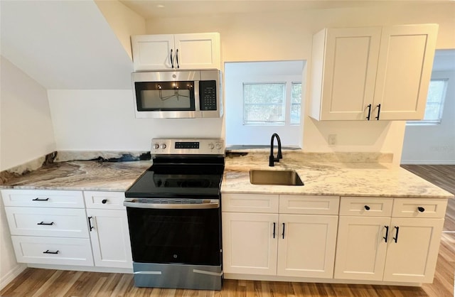 819 11th St N, Saint Petersburg, FL 33705 - kitchen with light wood-type flooring, a sink, light stone counters, white cabinetry, and appliances with stainless steel finishes
