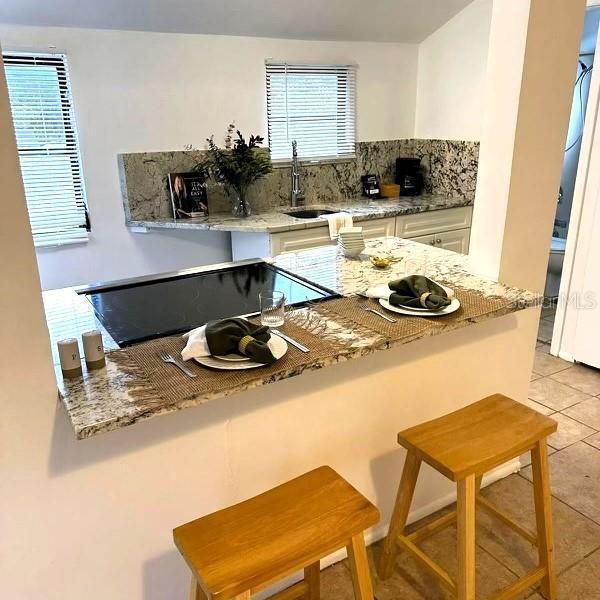 819 11th St N, Saint Petersburg, FL 33705 - kitchen featuring light stone counters, decorative backsplash, light tile patterned flooring, white cabinets, and a sink
