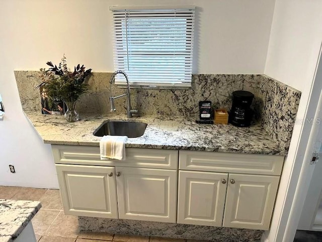 819 11th St N, Saint Petersburg, FL 33705 - kitchen with light stone counters, light tile patterned flooring, white cabinetry, and a sink