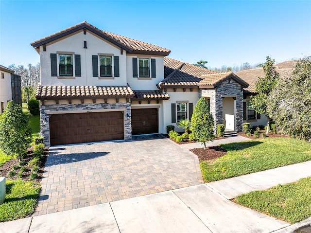 mediterranean / spanish house featuring an attached garage, stone siding, a tile roof, stucco siding, and decorative driveway