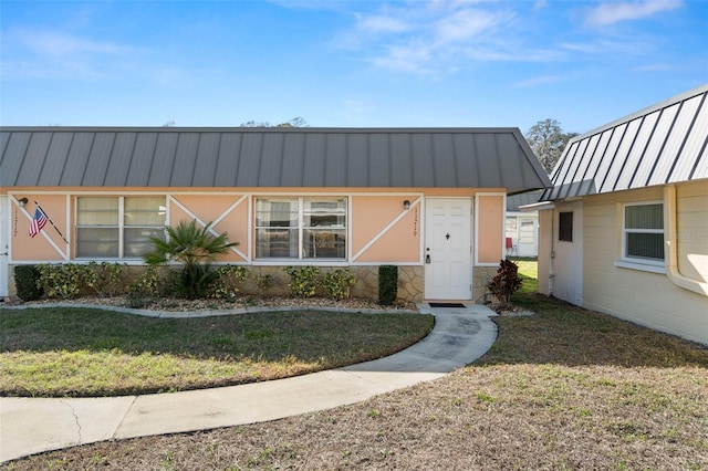 view of front facade with metal roof, concrete block siding, a front yard, and a standing seam roof