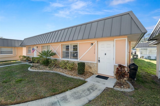 view of front of property featuring a standing seam roof, a front yard, stone siding, and metal roof