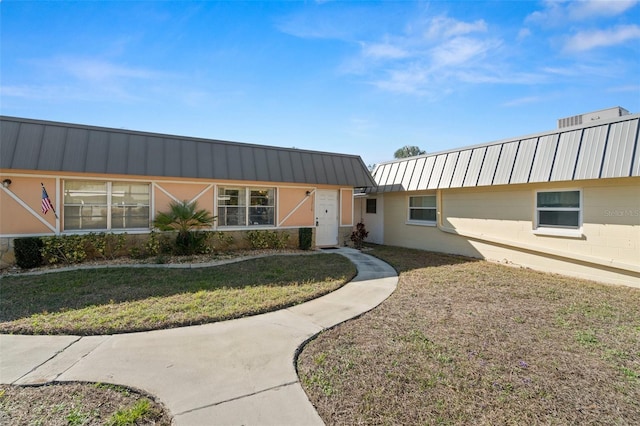 view of front of property featuring concrete block siding, a front lawn, and metal roof