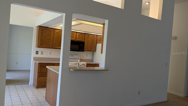 kitchen featuring brown cabinetry, baseboards, range with electric cooktop, light countertops, and black microwave