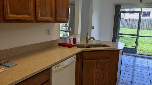 kitchen featuring brown cabinetry, a sink, a peninsula, and white dishwasher