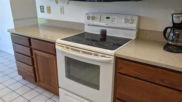 kitchen with white range with electric stovetop, light tile patterned floors, light countertops, and brown cabinetry