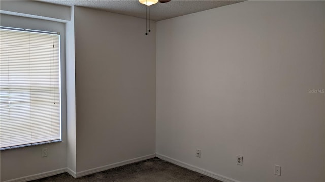 spare room with a ceiling fan, baseboards, dark colored carpet, and a textured ceiling