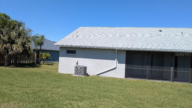 view of side of property featuring central air condition unit, a yard, roof with shingles, and stucco siding