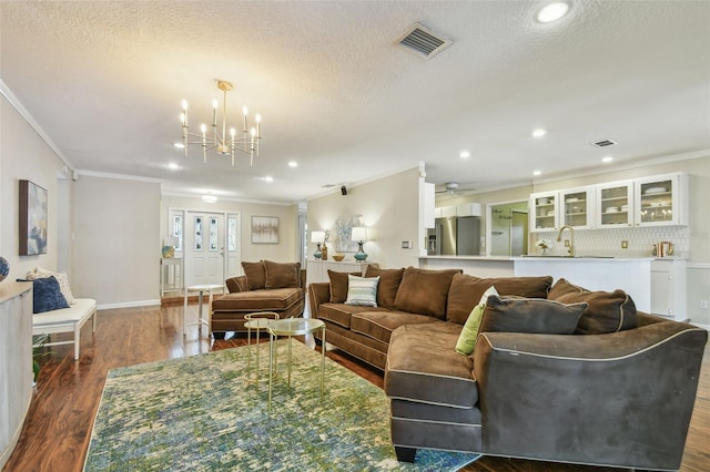 living room featuring crown molding, visible vents, an inviting chandelier, and dark wood finished floors