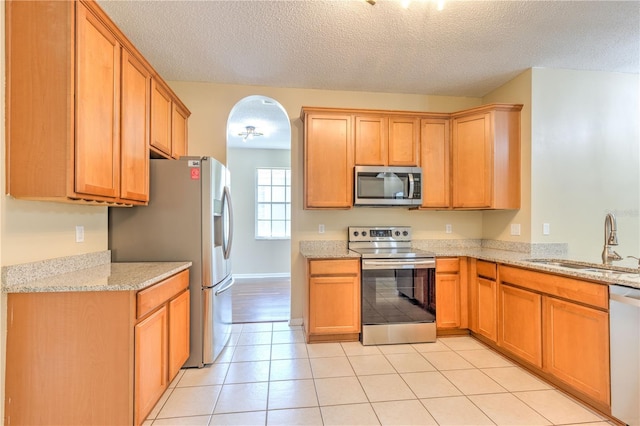 kitchen with a sink, stainless steel appliances, arched walkways, and light stone counters