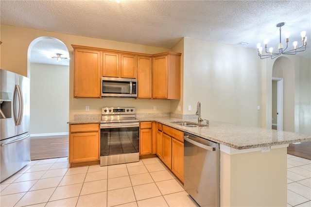 kitchen with light stone counters, appliances with stainless steel finishes, a peninsula, light tile patterned flooring, and a sink