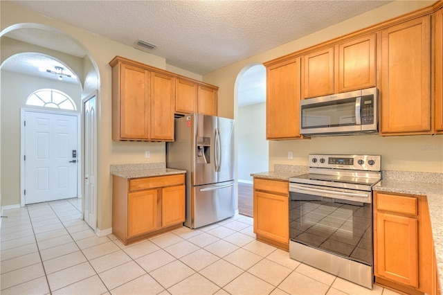 kitchen with light tile patterned flooring, visible vents, arched walkways, and stainless steel appliances