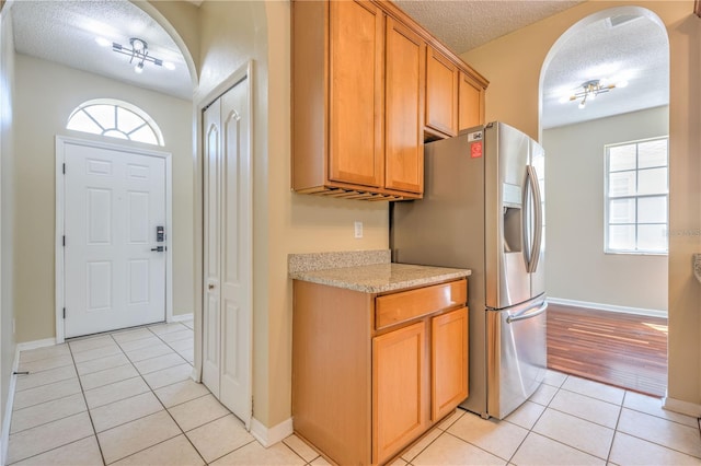 kitchen featuring a textured ceiling, arched walkways, light tile patterned flooring, light countertops, and a healthy amount of sunlight