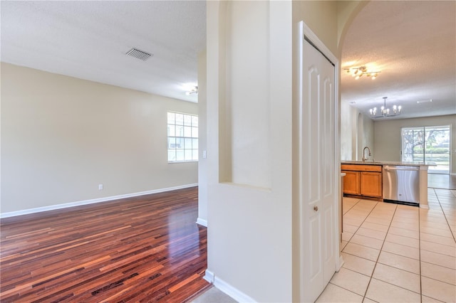 corridor featuring visible vents, a sink, a textured ceiling, an inviting chandelier, and light tile patterned flooring