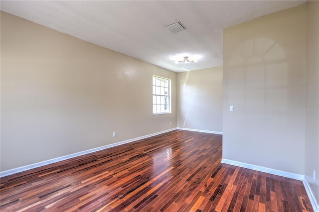 empty room with visible vents, baseboards, a textured ceiling, and dark wood-style floors