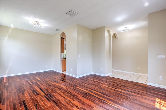 unfurnished room featuring wood finished floors, visible vents, arched walkways, and baseboards