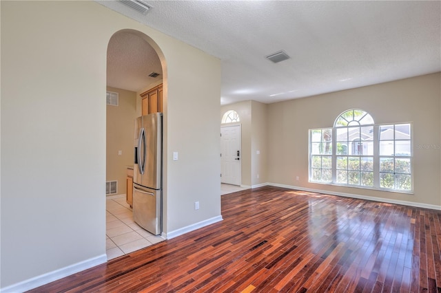 unfurnished room featuring a textured ceiling, arched walkways, visible vents, and light wood-type flooring