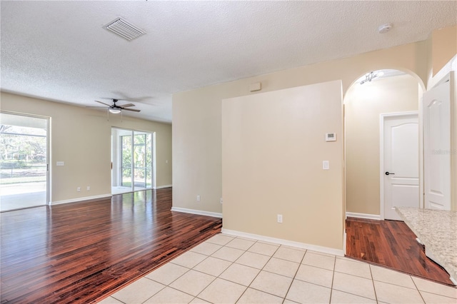 spare room with a ceiling fan, visible vents, light tile patterned flooring, arched walkways, and a textured ceiling