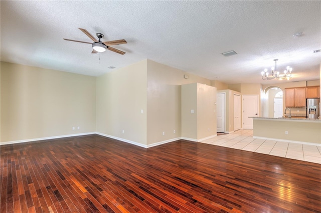 unfurnished living room with light wood finished floors, visible vents, baseboards, ceiling fan with notable chandelier, and a textured ceiling