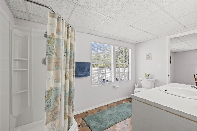 full bath featuring curtained shower, baseboards, a drop ceiling, toilet, and vanity