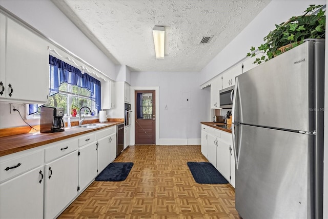 kitchen with a sink, white cabinets, appliances with stainless steel finishes, a textured ceiling, and wood counters