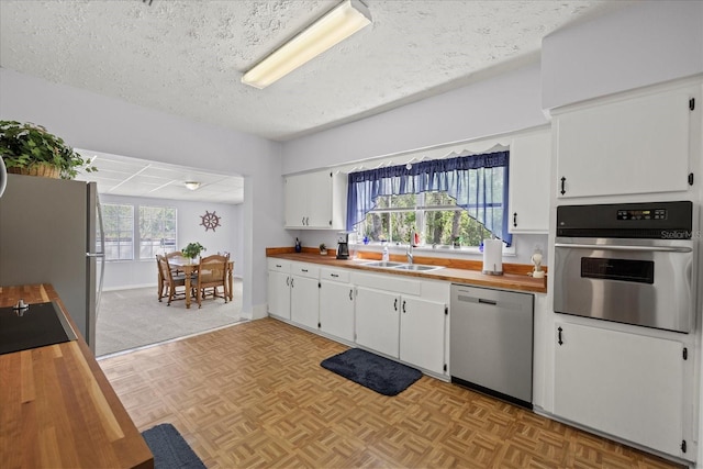 kitchen with a sink, appliances with stainless steel finishes, white cabinets, and butcher block counters