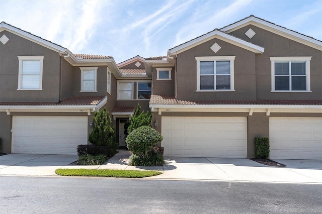 townhome / multi-family property featuring stucco siding, driveway, an attached garage, and a tiled roof