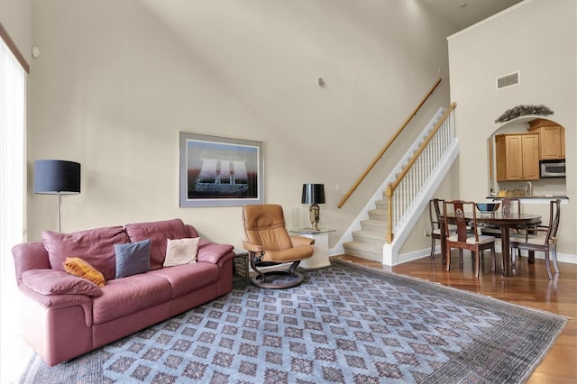 living room featuring visible vents, baseboards, stairs, a high ceiling, and wood finished floors