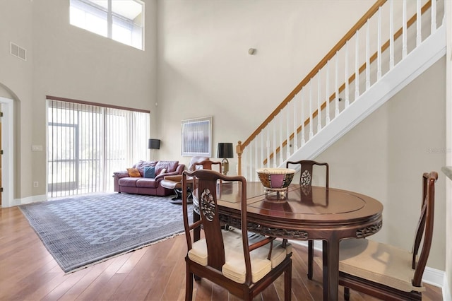 dining area featuring visible vents, baseboards, a high ceiling, wood finished floors, and arched walkways