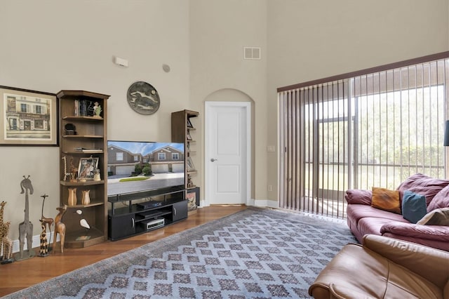 living room featuring wood finished floors, visible vents, a towering ceiling, and baseboards
