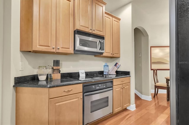 kitchen featuring baseboards, light brown cabinetry, light wood-style flooring, arched walkways, and stainless steel appliances