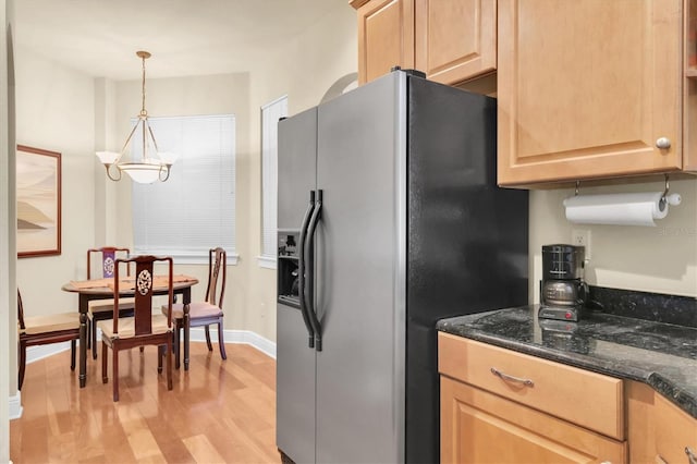 kitchen featuring dark stone countertops, light brown cabinets, an inviting chandelier, refrigerator with ice dispenser, and light wood-type flooring