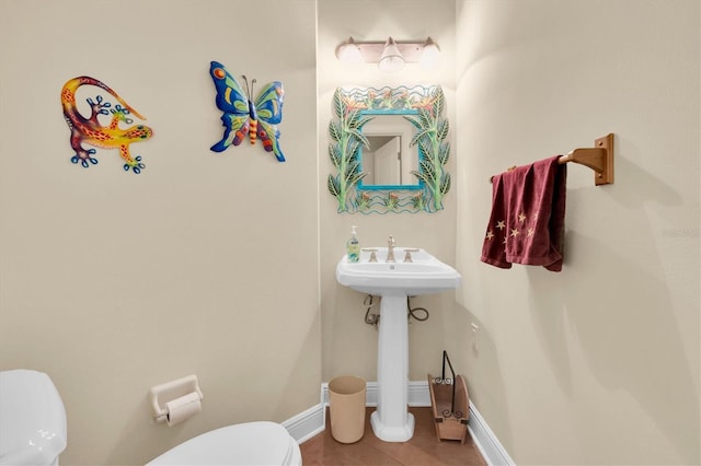 half bath featuring tile patterned floors, toilet, baseboards, and a sink